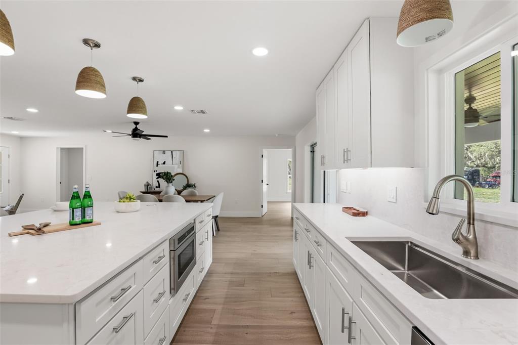 A bright, modern kitchen features white cabinetry, quartz countertops, a large island, and wood flooring — 39251 COUNTY ROAD 439, UMATILLA, FL