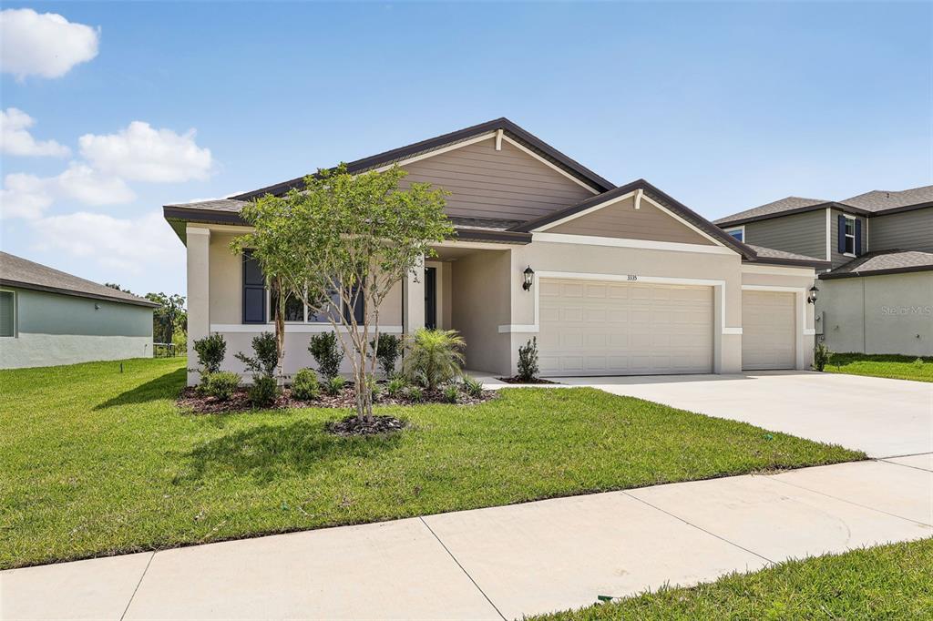 A single-story suburban house features a tan stucco exterior, a two-car garage, and a lawn — 3335 ORCHARD LOOP, BARTOW, FL