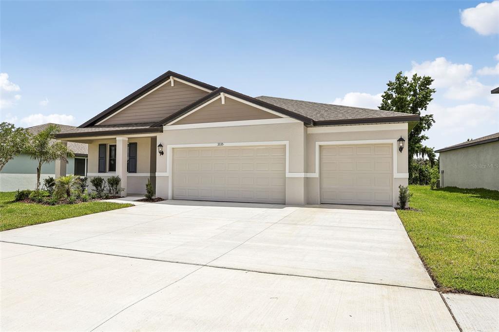 A single-story house with a three-car garage and a concrete driveway under a blue sky — 3335 ORCHARD LOOP, BARTOW, FL