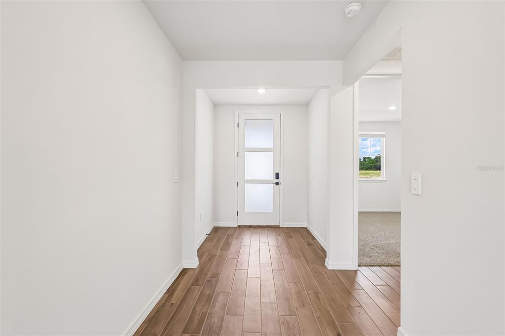 A bright entryway features white walls, wood-look tile flooring, and a modern glass-paneled front door — 3335 ORCHARD LOOP, BARTOW, FL