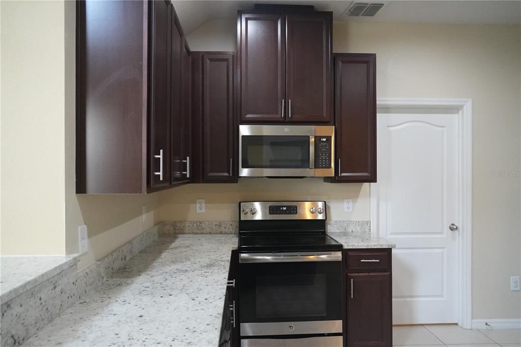 A kitchen features dark wood cabinets, stainless steel appliances, and speckled granite countertops — 2212 LENNOX DALE LANE, BRANDON, FL