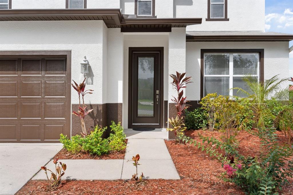 A white house exterior features a brown garage door, a glass-paneled front door, and landscaping — 5424 HAMMOCK VIEW LANE, APOLLO BEACH, FL
