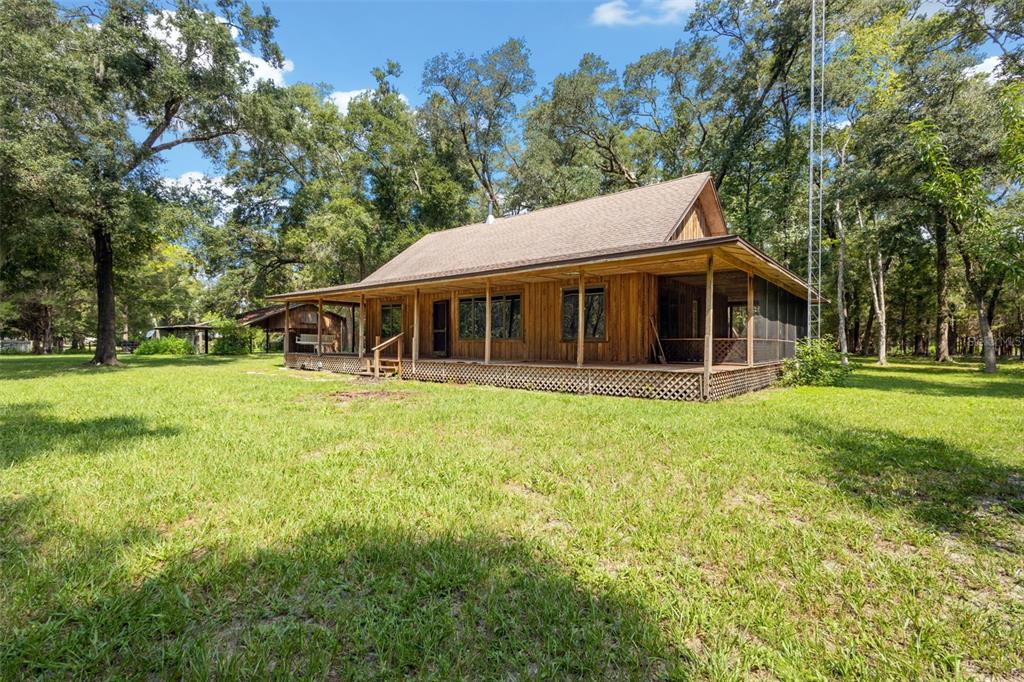 A wooden cabin with a wrap-around porch sits on a grassy lot surrounded by trees — 5581 NE 157TH TERRACE, WILLISTON, FL