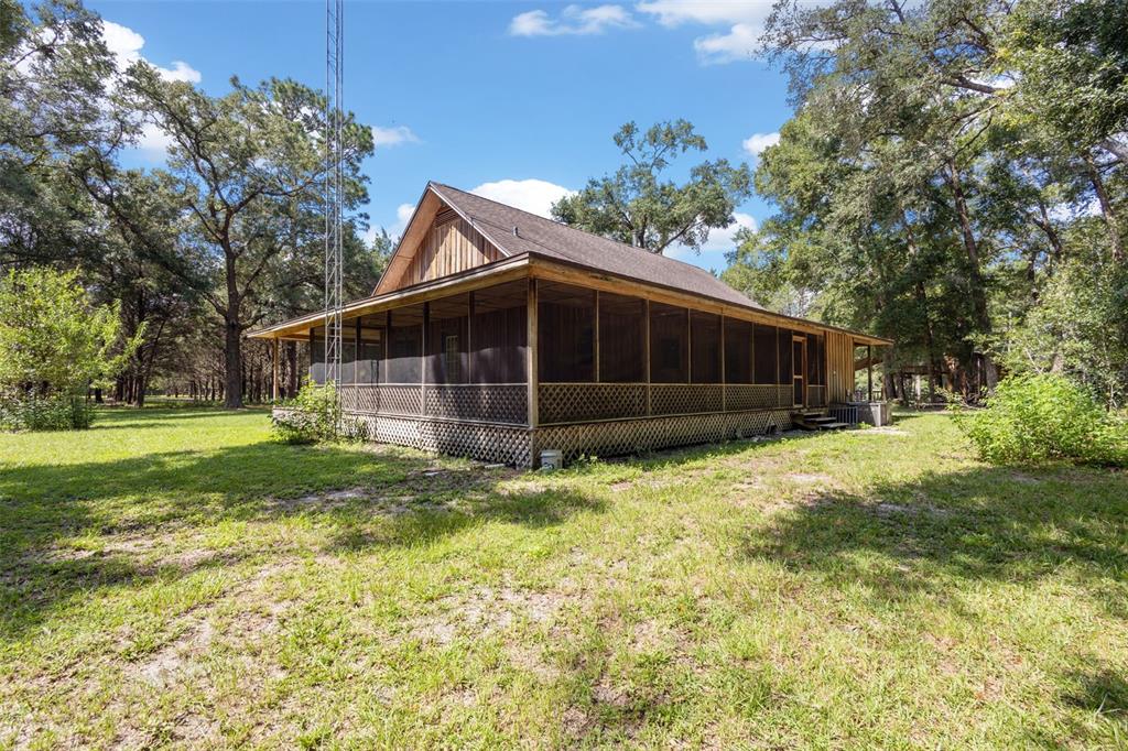 A wooden house with a wrap-around screened porch sits in a grassy, wooded lot — 5581 NE 157TH TERRACE, WILLISTON, FL