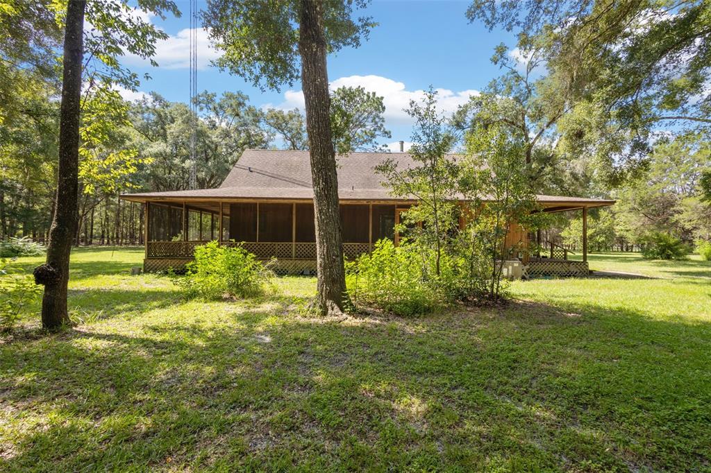 A wooden house with a wrap-around screened porch sits in a wooded, grassy yard — 5581 NE 157TH TERRACE, WILLISTON, FL