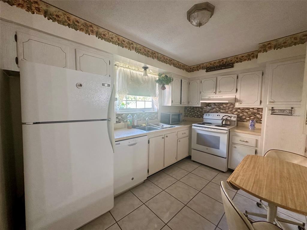 A kitchen with white cabinets, white appliances, tiled floors, and a floral wallpaper border — 4115 34TH WAY S UNIT 194, ST PETERSBURG, FL