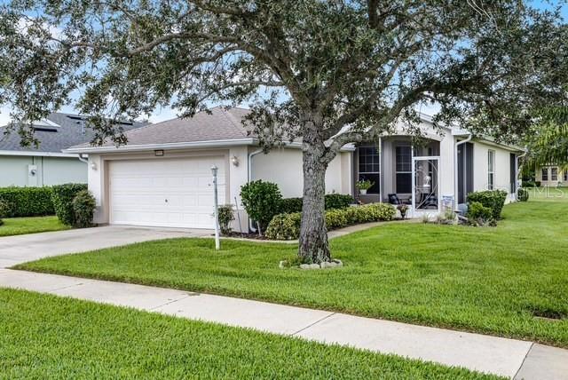 A single-story house with a two-car garage and a large tree in the front yard — 27111 NOSTALGIA DRIVE, LEESBURG, FL