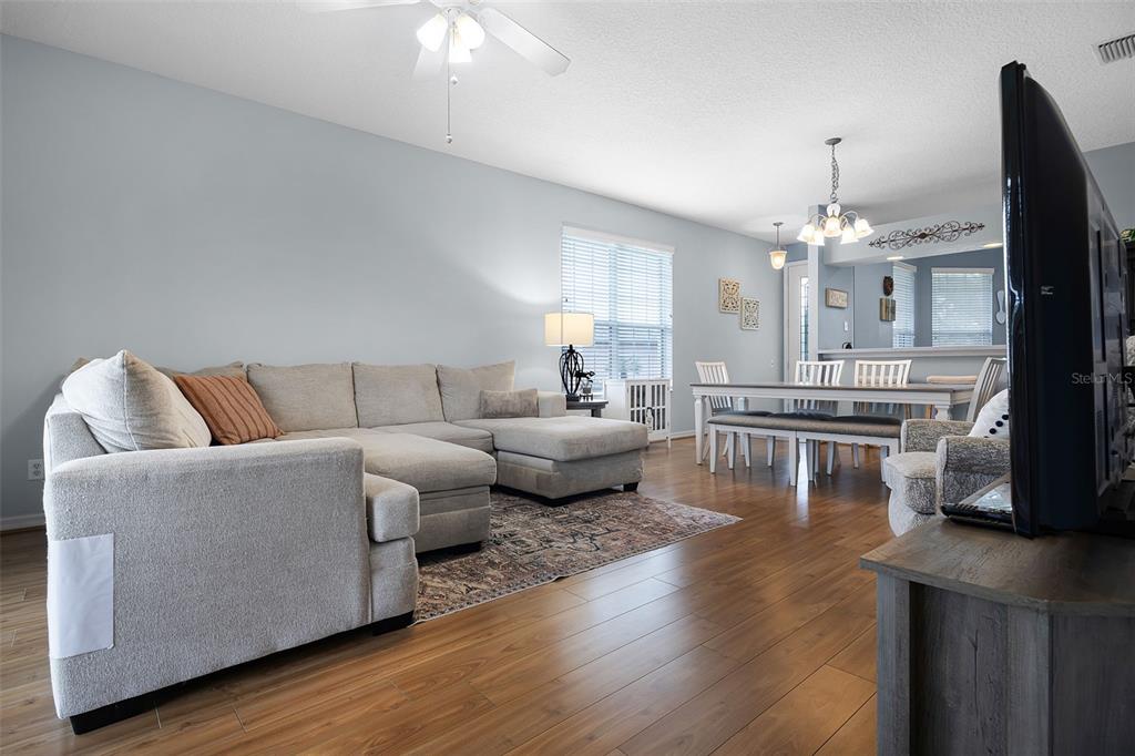 A living room with a sectional sofa, dining area, and wood-look flooring — 27111 NOSTALGIA DRIVE, LEESBURG, FL
