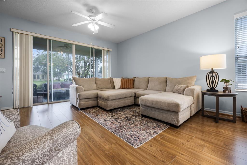 A living room features a large sectional sofa, a patterned area rug, and sliding glass doors — 27111 NOSTALGIA DRIVE, LEESBURG, FL