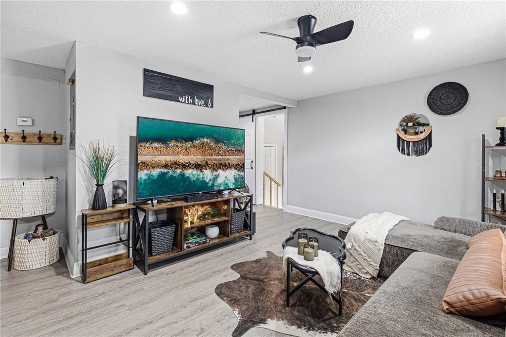 A living room features a television on a rustic stand, a sectional sofa, and flooring — 7709 PASCHAL STREET, JACKSONVILLE, FL