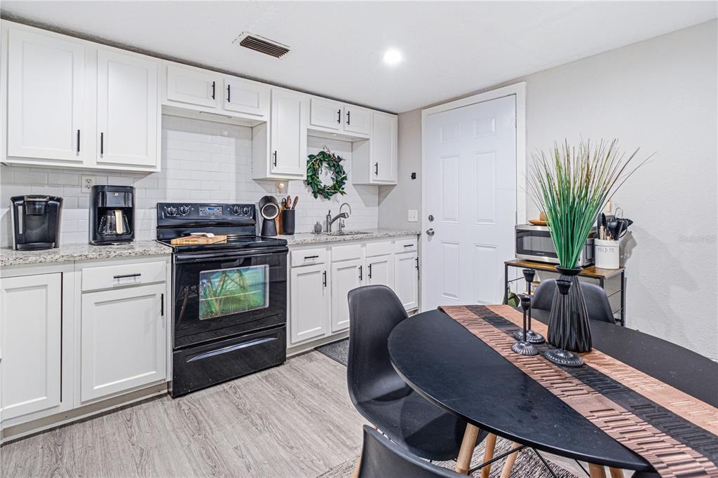 A kitchen features white cabinets, black appliances, granite countertops, and a small dining table — 7709 PASCHAL STREET, JACKSONVILLE, FL