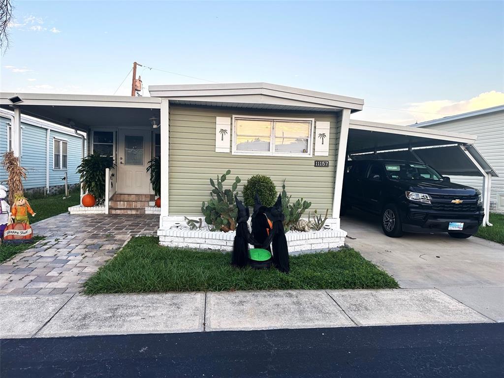 A light green manufactured home features a carport, a brick-bordered garden, and Halloween decorations — 11157 102ND WAY UNIT 213, LARGO, FL