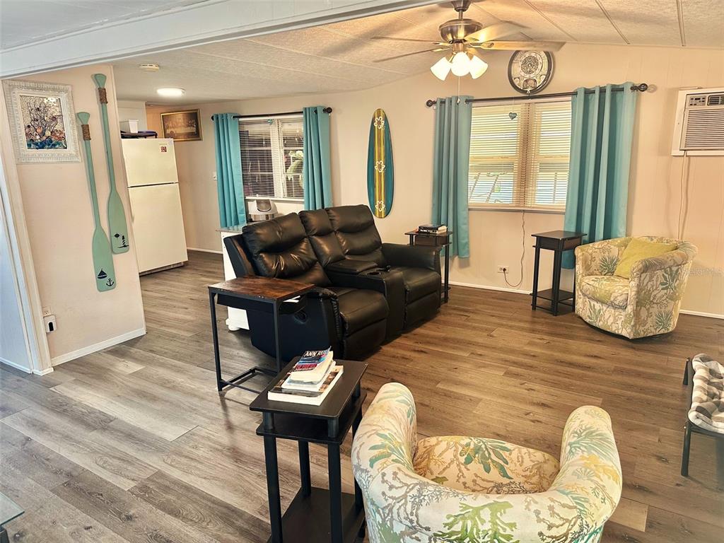 A living room with wood-look flooring, a black leather loveseat, and two patterned armchairs — 11157 102ND WAY UNIT 213, LARGO, FL