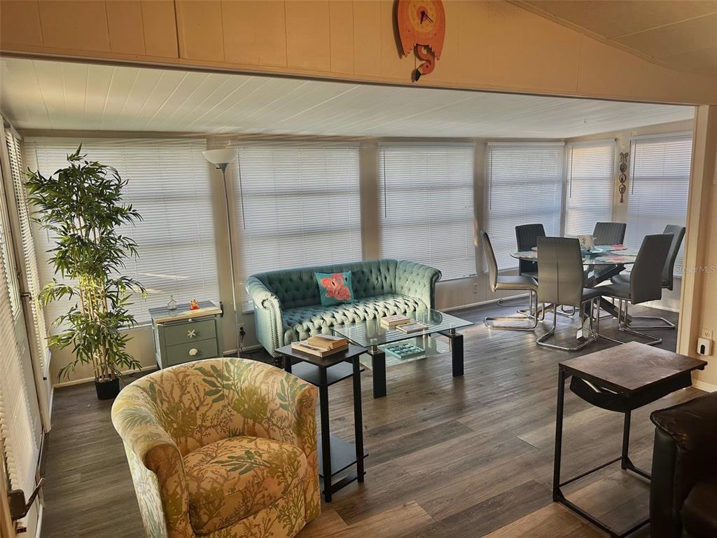 A sunroom features a teal tufted sofa, a patterned armchair, and a glass dining table — 11157 102ND WAY UNIT 213, LARGO, FL