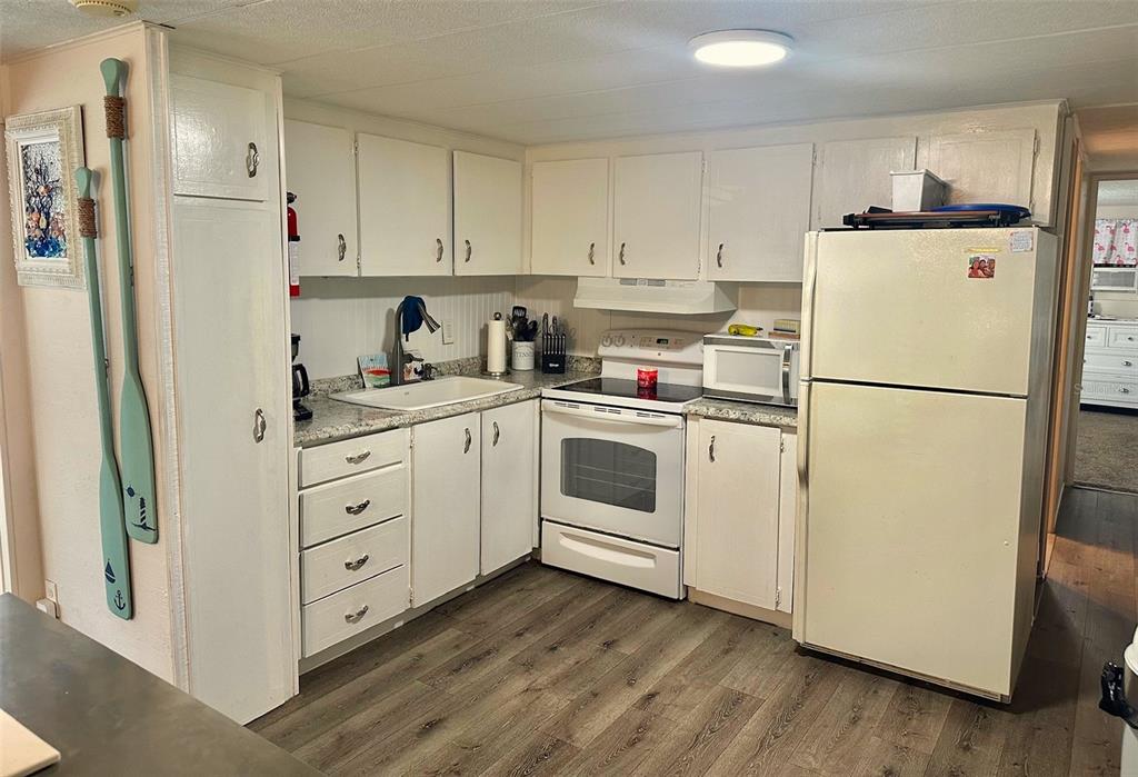 A kitchen with white cabinets, light countertops, white appliances, and wood-look flooring — 11157 102ND WAY UNIT 213, LARGO, FL