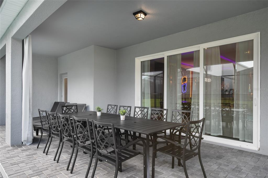 A covered outdoor patio features a long black dining table with chairs on a paver floor — 16364 SAINT KITTS CIRCLE, CLERMONT, FL