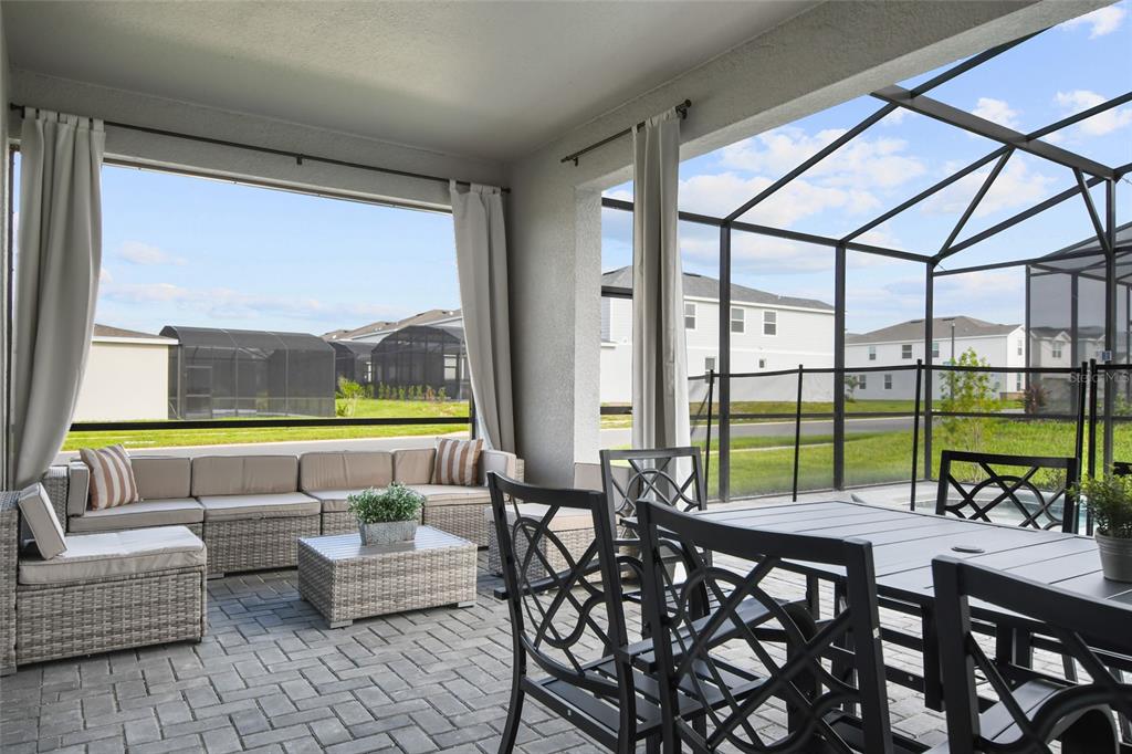 A covered patio features wicker furniture, a dining set, and a screened-in enclosure overlooking houses — 16364 SAINT KITTS CIRCLE, CLERMONT, FL