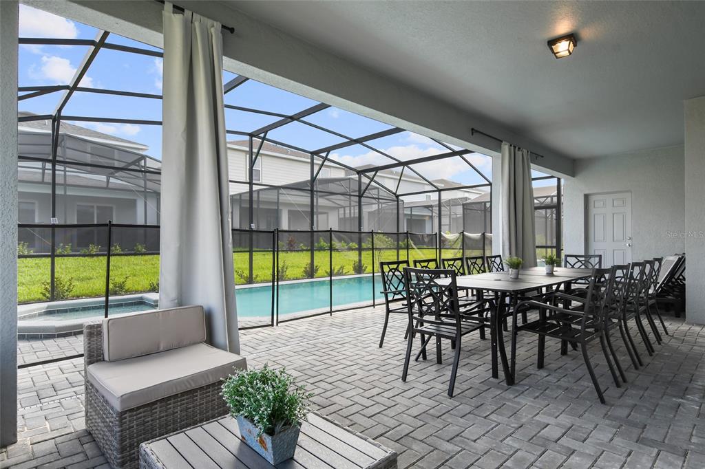 A covered patio features a dining set, lounge chair, and a screened-in pool area — 16364 SAINT KITTS CIRCLE, CLERMONT, FL