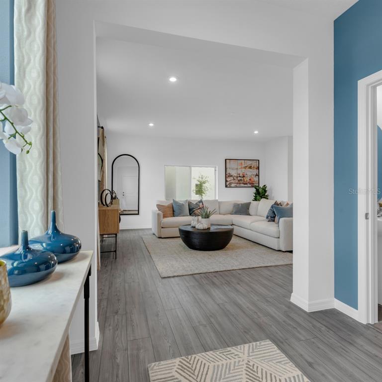 A view from a hallway into a living room with a sectional sofa and wood flooring — 3957 PENTAS ROAD, TAVARES, FL