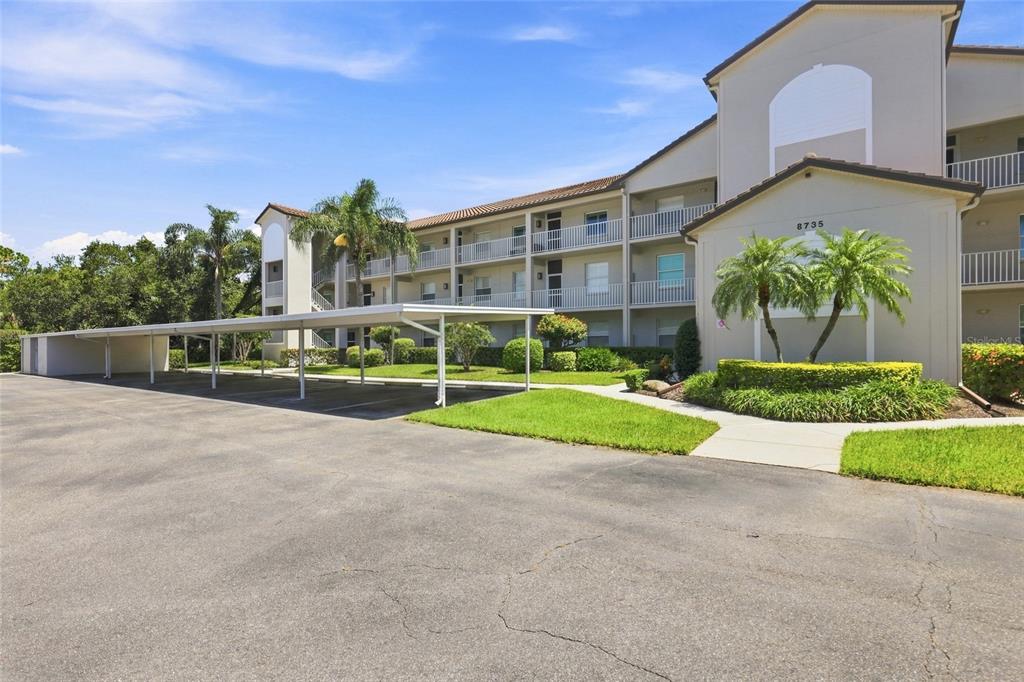 A multi-story apartment building features a covered parking area and landscaped grounds — 8735 OLDE HICKORY AVENUE UNIT 8304, SARASOTA, FL