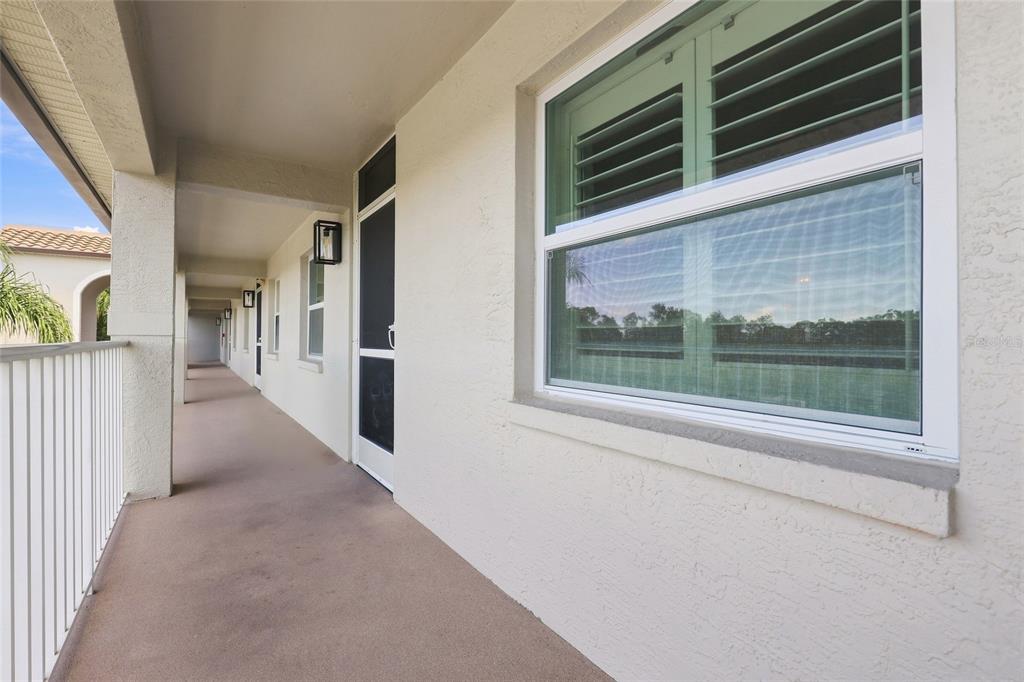 A covered outdoor balcony walkway with a white railing, beige walls, and a window — 8735 OLDE HICKORY AVENUE UNIT 8304, SARASOTA, FL