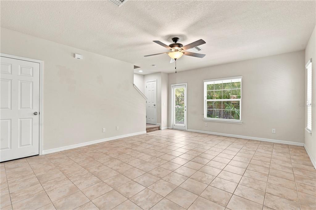 An empty living room features light-colored tile flooring, beige walls, a ceiling fan, and windows — 4824 CHATTERTON WAY, RIVERVIEW, FL