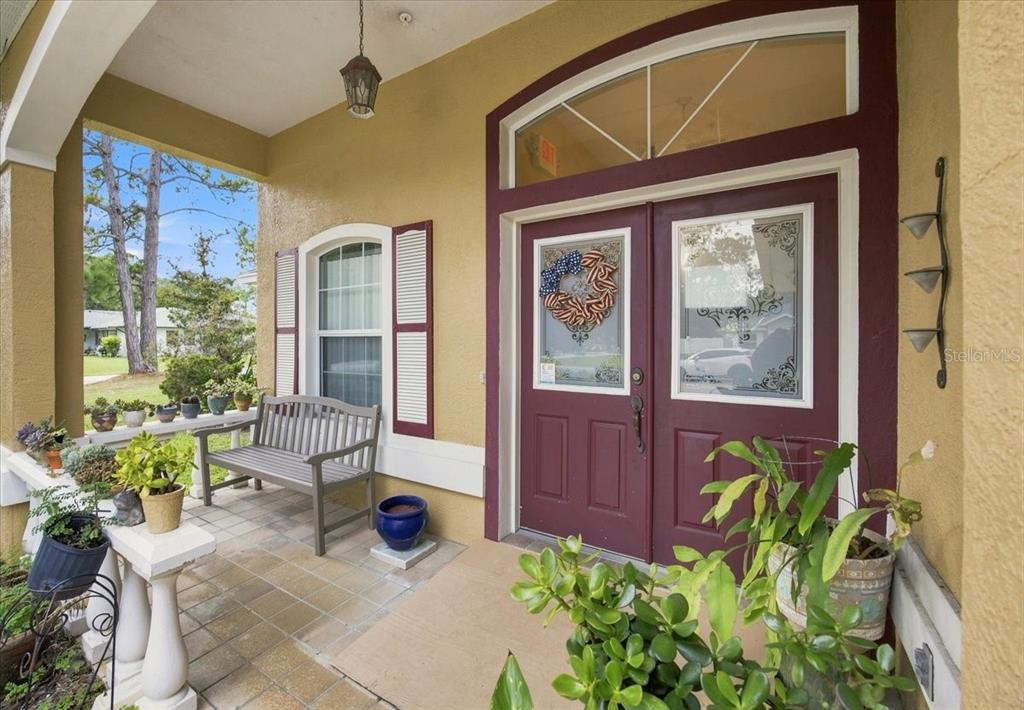 A covered front porch features a double door entry, a wooden bench, and potted plants — 1 PEBBLE WOOD LANE, PALM COAST, FL