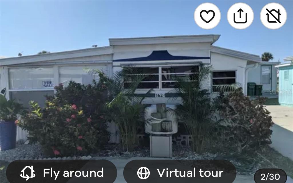 The exterior of a manufactured home features a front porch, landscaping, and a blue awning — 1475 FLAMINGO DRIVE UNIT 162, ENGLEWOOD, FL