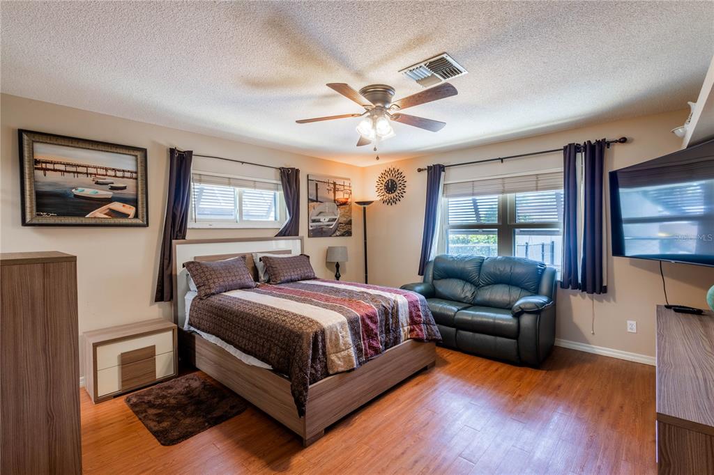 A bedroom features a bed, a dark green loveseat, wood-look flooring, and a ceiling fan — 404 N HERON STREET, SEBRING, FL