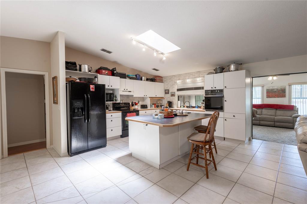 A kitchen features white cabinets, a black refrigerator, a central island, and tiled flooring — 404 N HERON STREET, SEBRING, FL