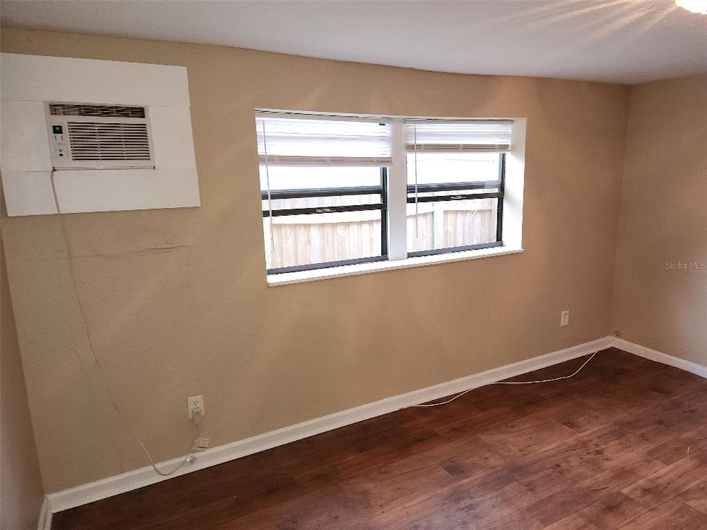 A room with wood-look flooring, beige walls, a window with blinds, and a wall-mounted air conditioner — 2135 8TH AVENUE N UNIT 2, ST PETERSBURG, FL