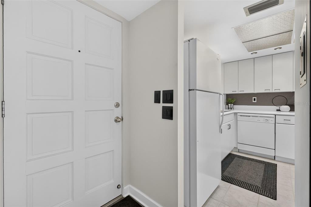 A white entry door stands next to a small kitchen with white cabinets and appliances — 101 N GRANDVIEW STREET UNIT 412, MOUNT DORA, FL