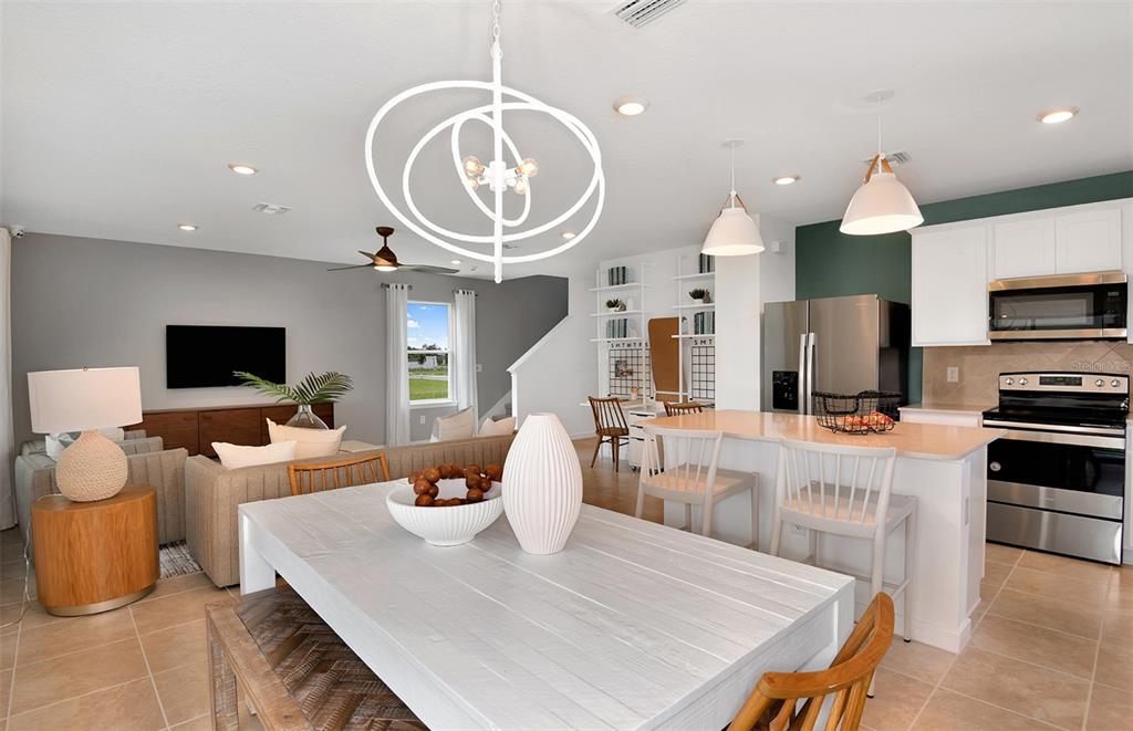An open-concept living and dining area features a white chandelier, kitchen island, and neutral decor — 10438 HIDDEN BANKS GLEN, PARRISH, FL