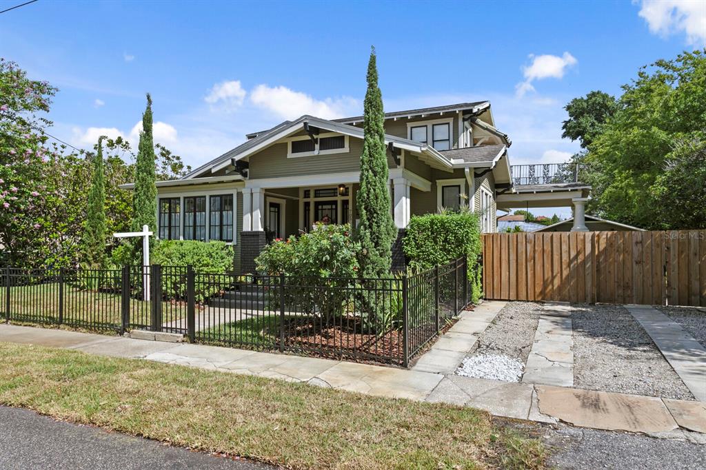 A green bungalow with a front porch, black metal fence, and a gravel driveway — 705 W WEST STREET, TAMPA, FL