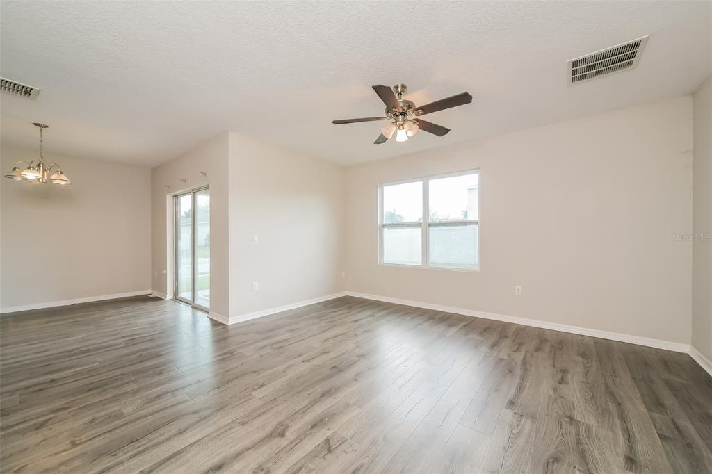 An empty living room features light gray wood-look flooring, a ceiling fan, and sliding glass doors — 2301 SEQUOIA WAY, DAVENPORT, FL