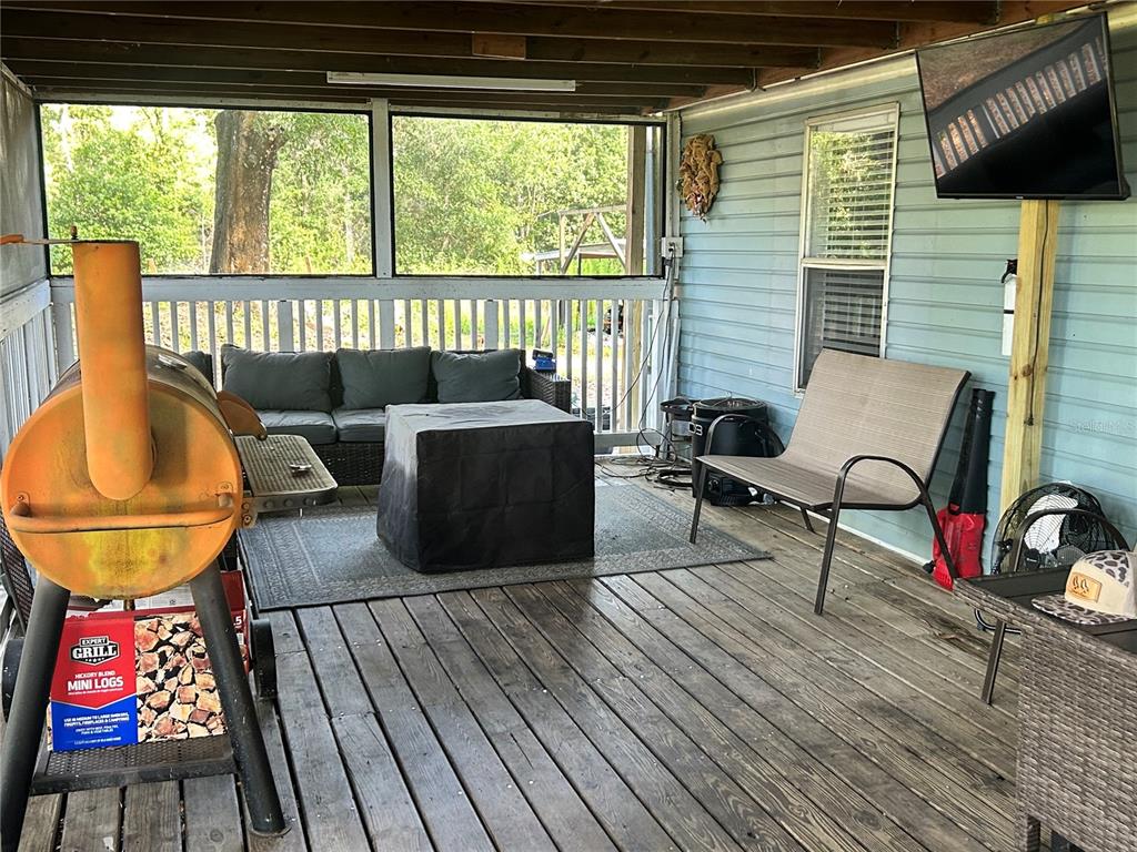 A covered wooden deck features a grill, outdoor seating, and a mounted television — 5237 TURTLE DOVE TRAIL, LAKELAND, FL