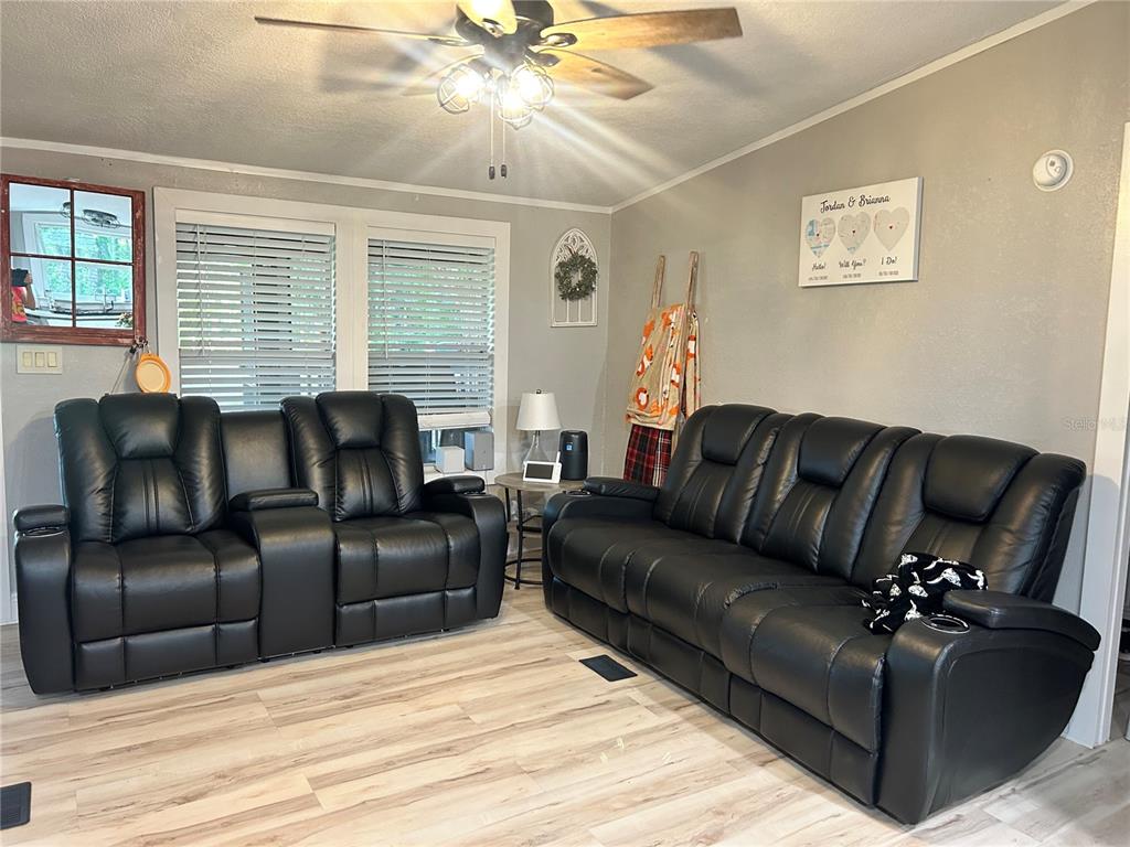 A living room features two black leather reclining sofas, light wood flooring, and a ceiling fan — 5237 TURTLE DOVE TRAIL, LAKELAND, FL