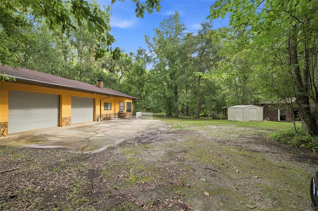 A yellow garage with two roll-up doors sits on a concrete driveway near wooded land — 16205 PERIMETER DRIVE, BROOKSVILLE, FL