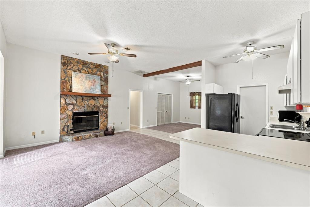 A living room with a stone fireplace and carpeted floor opens to a tiled kitchen area — 16205 PERIMETER DRIVE, BROOKSVILLE, FL