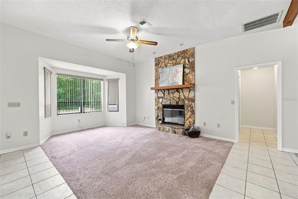 A living room features a stone fireplace, carpeted flooring, a ceiling fan, and a bay window — 16205 PERIMETER DRIVE, BROOKSVILLE, FL