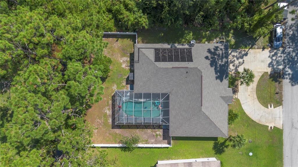 An aerial view shows a house with a pool enclosure, solar panels, and a fenced yard — 57 RYARBOR DRIVE, PALM COAST, FL
