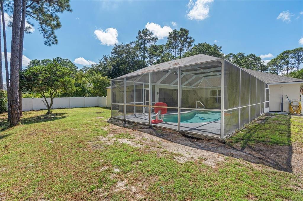 A backyard features a screened-in swimming pool enclosure, a small tree, and a white fence — 57 RYARBOR DRIVE, PALM COAST, FL