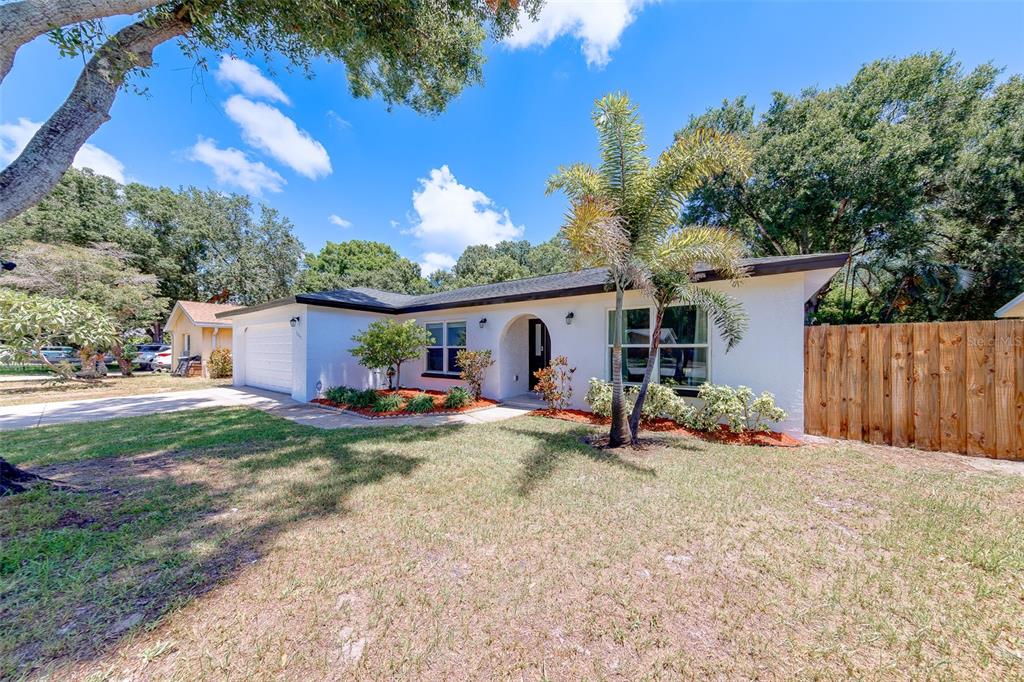 A single-story white house with a garage, palm tree, and wooden fence under a blue sky — 2043 DODGE STREET, CLEARWATER, FL