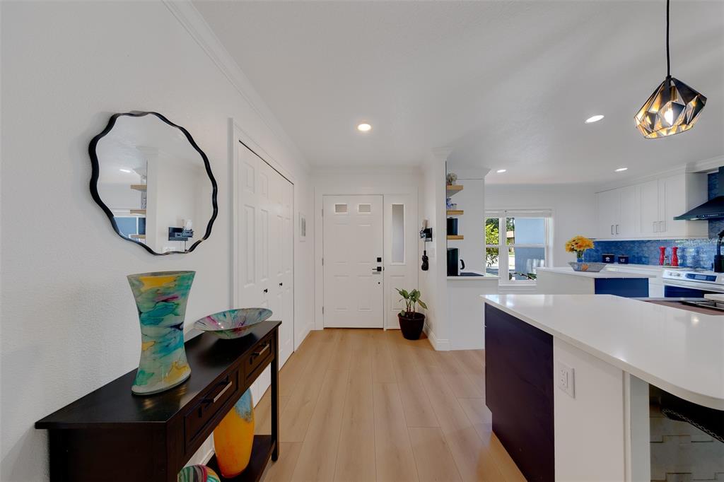 A bright entryway leads into a kitchen with white cabinets and a dark kitchen island — 2043 DODGE STREET, CLEARWATER, FL