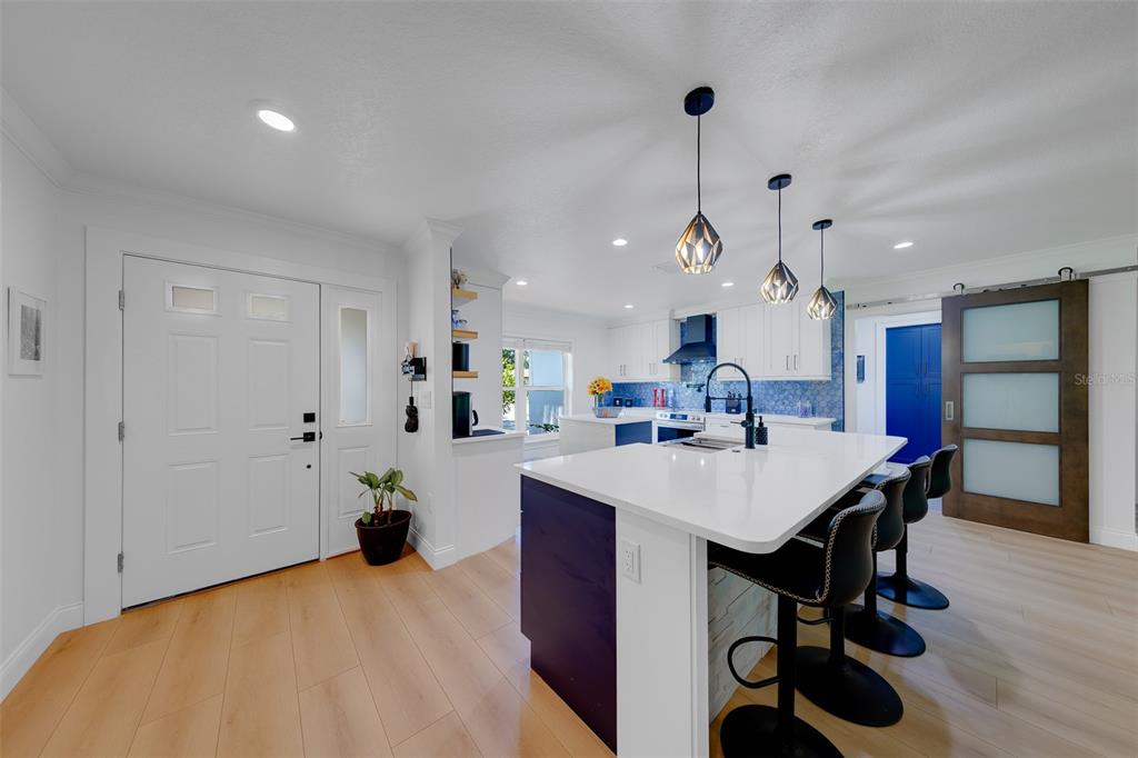 A modern kitchen features a white island with bar seating, blue cabinetry, and light wood flooring — 2043 DODGE STREET, CLEARWATER, FL