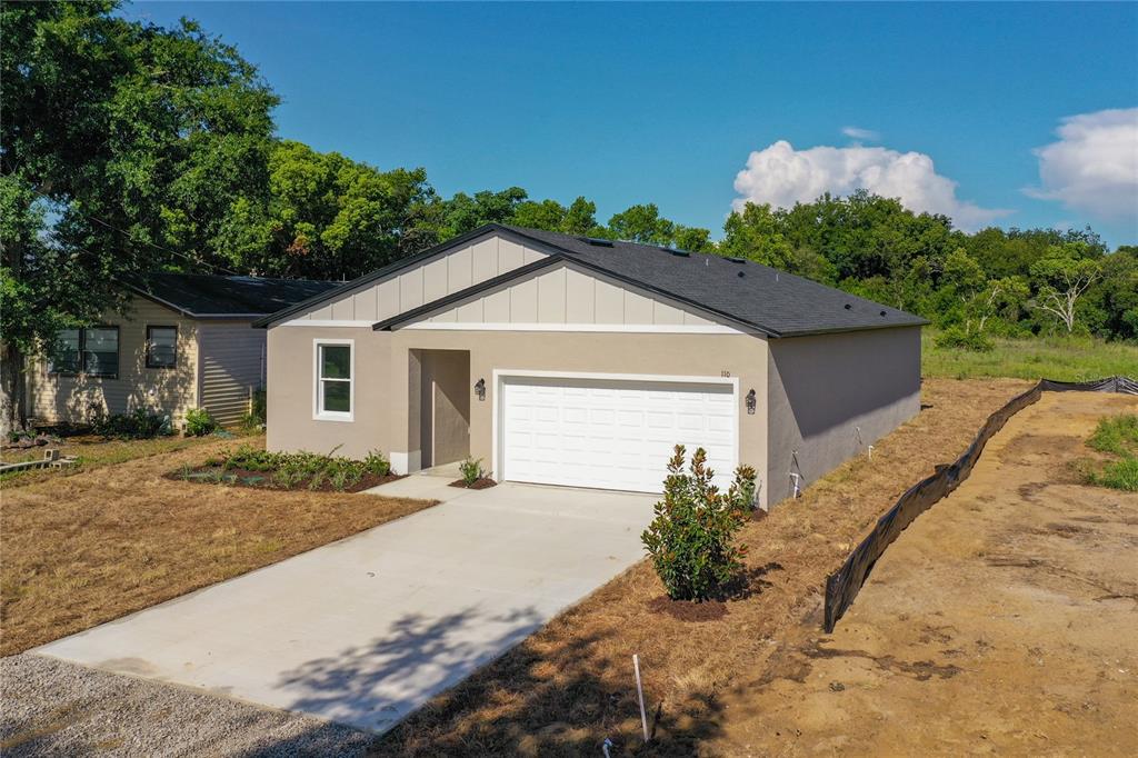 A newly constructed single-story house with a white garage door and beige stucco exterior — 110 FRUITWOOD AVENUE, EUSTIS, FL