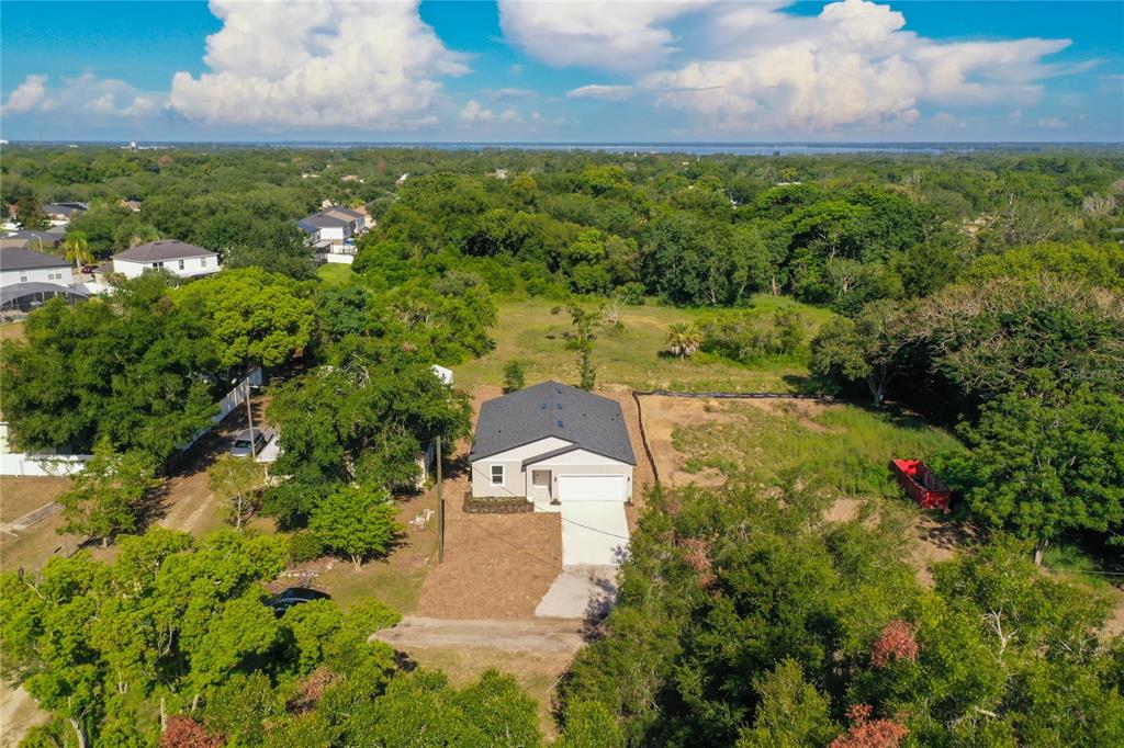 An aerial view shows a newly constructed single-story house situated on a large, wooded lot — 110 FRUITWOOD AVENUE, EUSTIS, FL