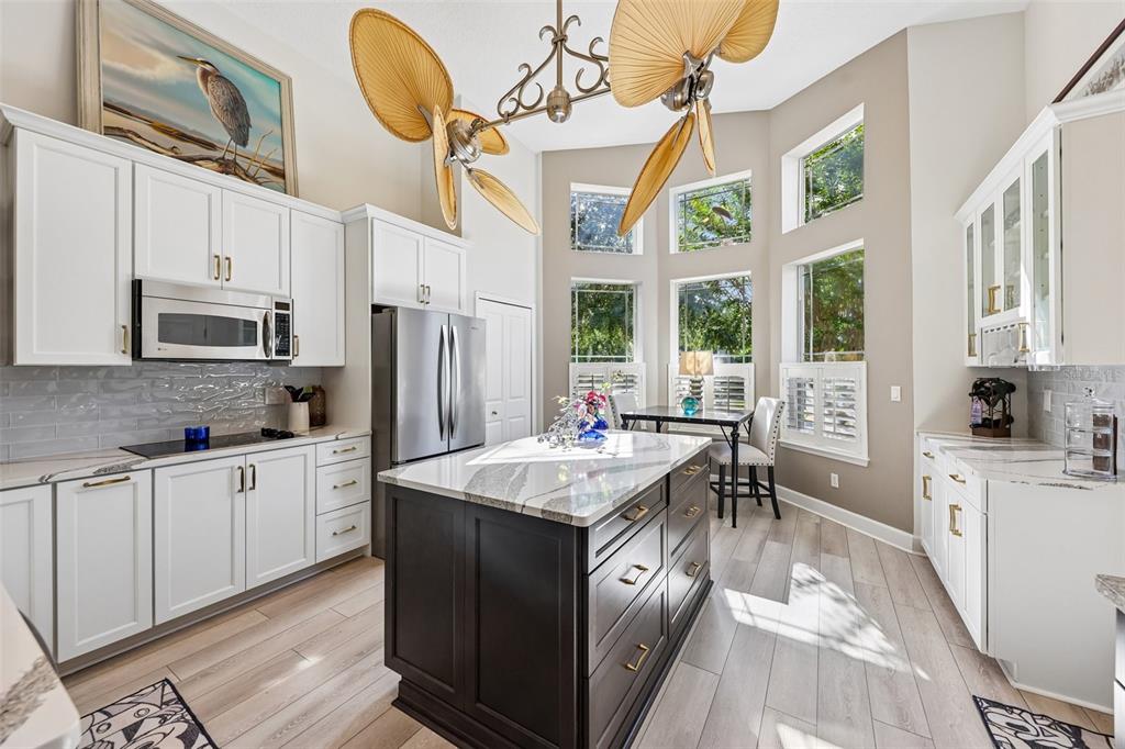 A kitchen features white cabinetry, a dark island, stainless steel appliances, and a palm-leaf ceiling fan — 456 CHELSEA PLACE AVENUE, ORMOND BEACH, FL
