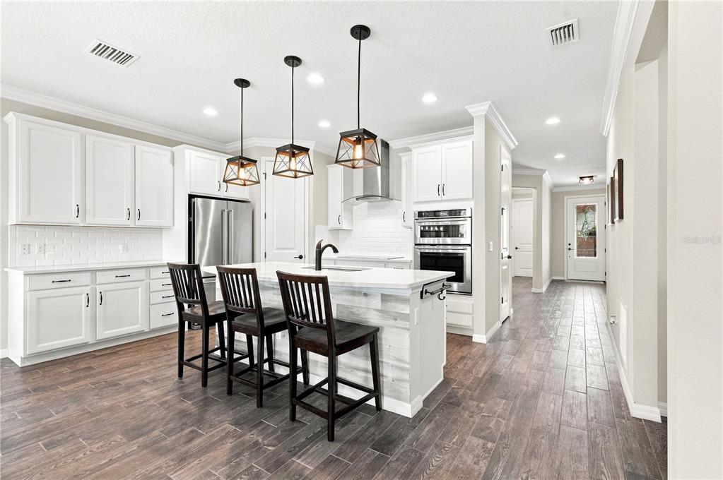 A modern kitchen features white cabinetry, a central island with bar seating, and wood-look flooring — 7278 TWILIGHT BAY DRIVE, WINTER GARDEN, FL