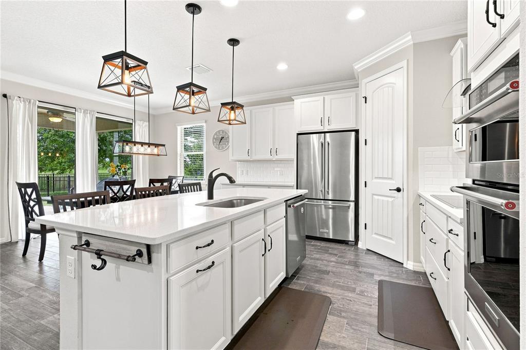 A bright kitchen features white cabinetry, a large quartz island, and stainless steel appliances — 7278 TWILIGHT BAY DRIVE, WINTER GARDEN, FL